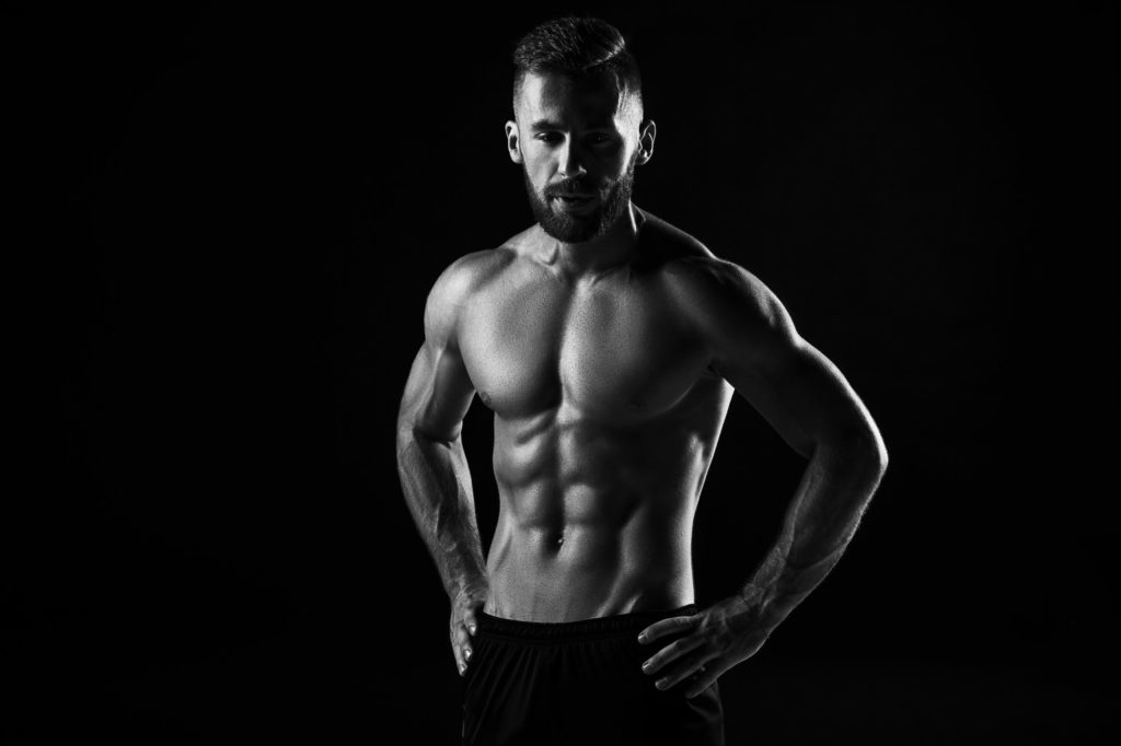 The torso of attractive male body builder on black background.