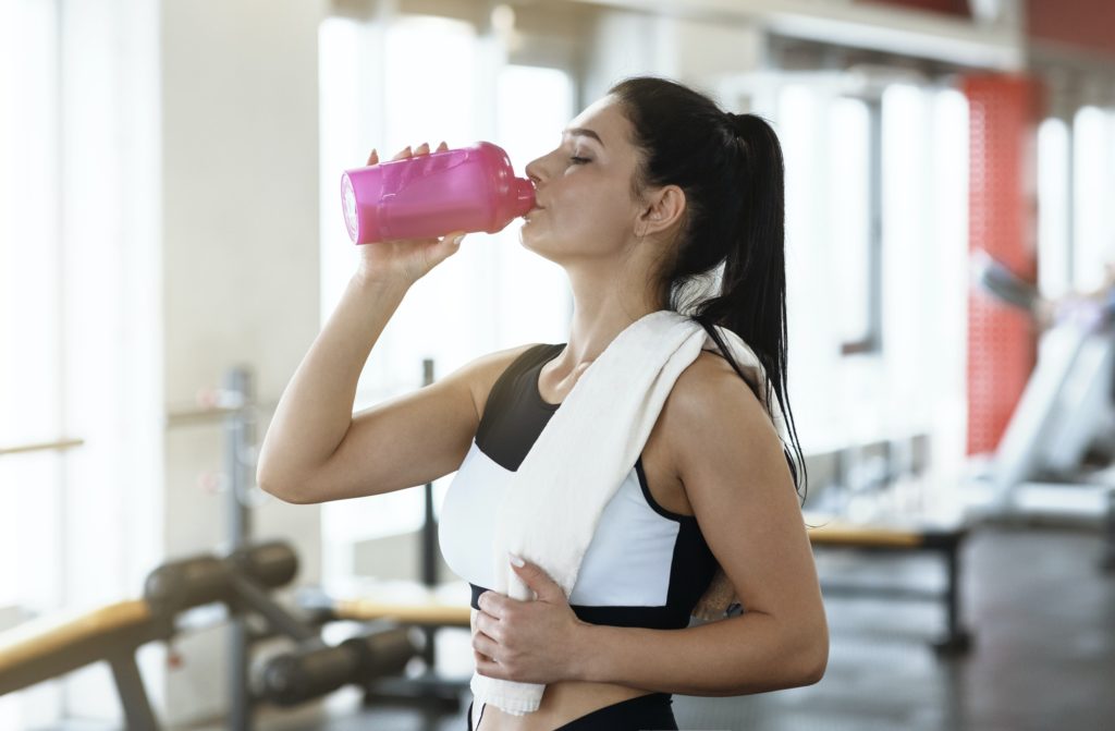 Keep hydrated. Young woman drinking water or protein cocktail in gym